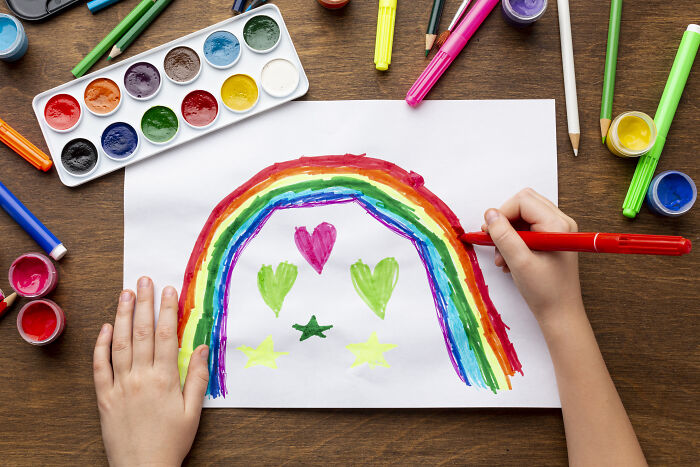 Child painting a colorful rainbow with hearts and stars, showcasing creative freedom in an art teachers online session.
