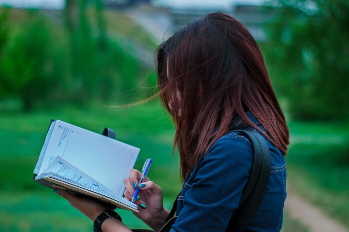 Young woman journaling outdoors, capturing moments of creative freedom shared by art teachers online.