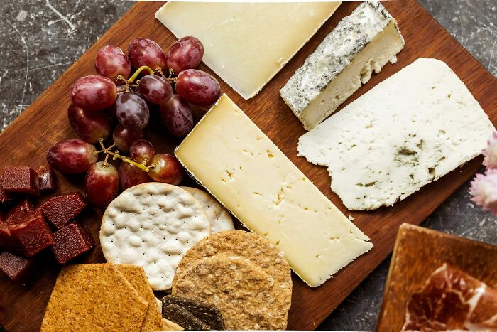 Assorted cheeses, grapes, and crackers on a wooden board illustrating police getting dragged into nonsense scenarios.