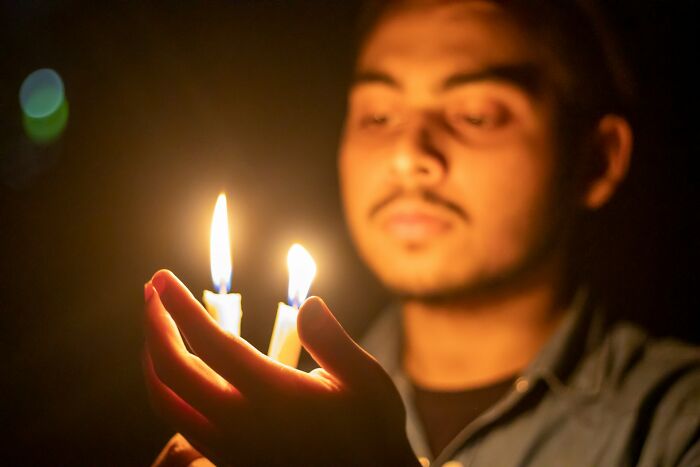 Young man holding two flickering candles in the dark, symbolizing reflection and epicly unhinged ways to get back at cheating exes.