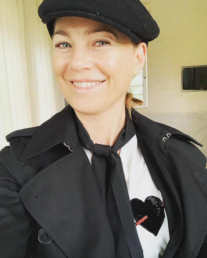 Ellen Pompeo smiling indoors wearing a black coat and hat, related to TSA and explosives squad airport incident.