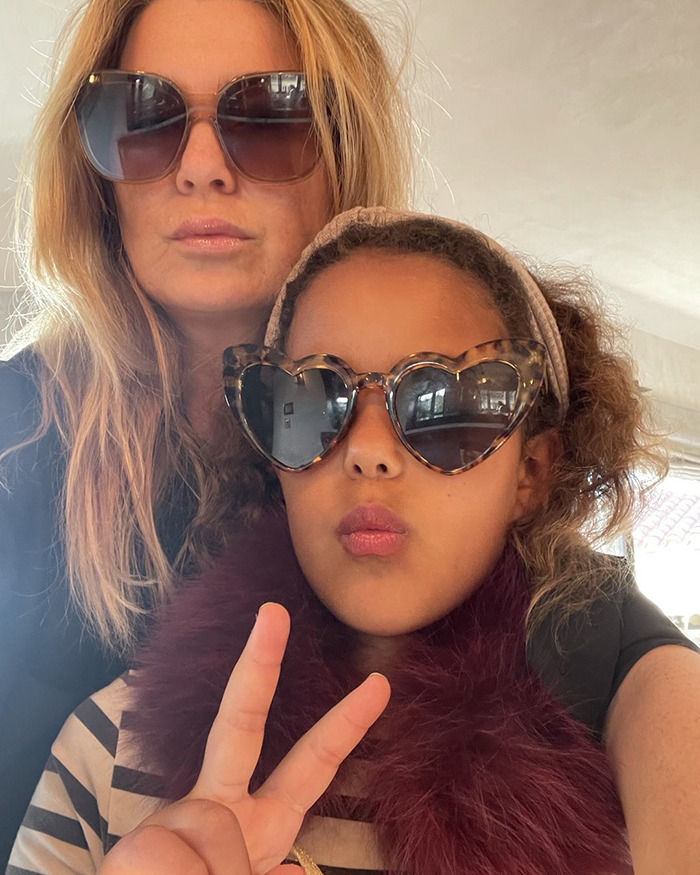 Ellen Pompeo wearing sunglasses and posing with a child wearing heart-shaped sunglasses and making a peace sign.