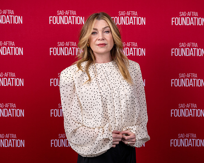 Ellen Pompeo in a white polka dot blouse posing in front of a red SAG-AFTRA Foundation backdrop at an event.