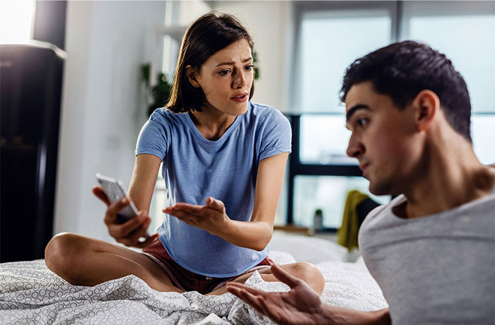 Couple having a tense conversation in bedroom with woman explaining, highlighting messy home and illness-related cleaning issues.