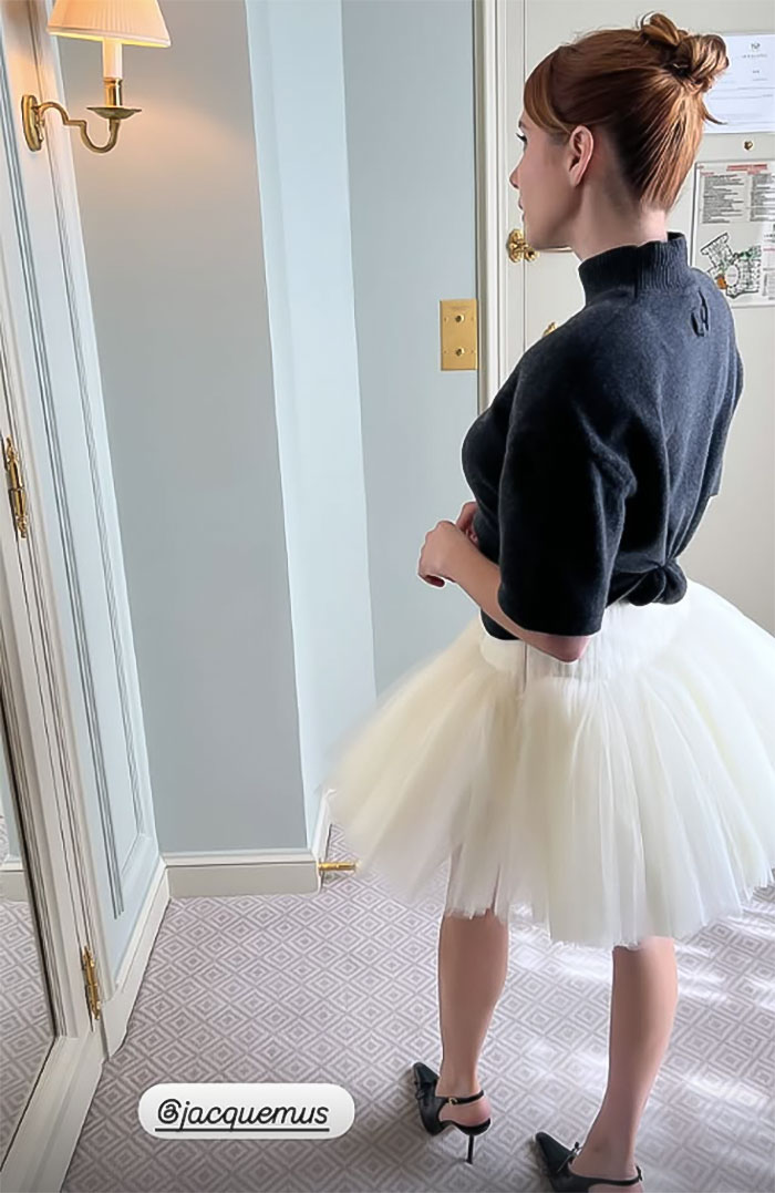 Woman in a black sweater and white tulle skirt, posing indoors with a stylish updo hairstyle. Woman in a black sweater and white tulle skirt, posing indoors with a stylish updo hairstyle.