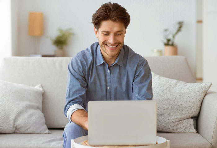 Young worker sitting on a couch, smiling while using a laptop, symbolizing changing attitudes in career advice situations.