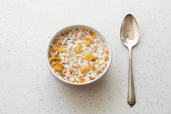 Bowl of cereal with milk next to a spoon on a speckled white countertop, featuring completely legal total psychopath theme.