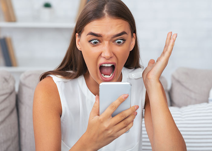 Woman shocked and frustrated while looking at her phone, reacting to friend wanting her to cancel kid&rsquo;s party.