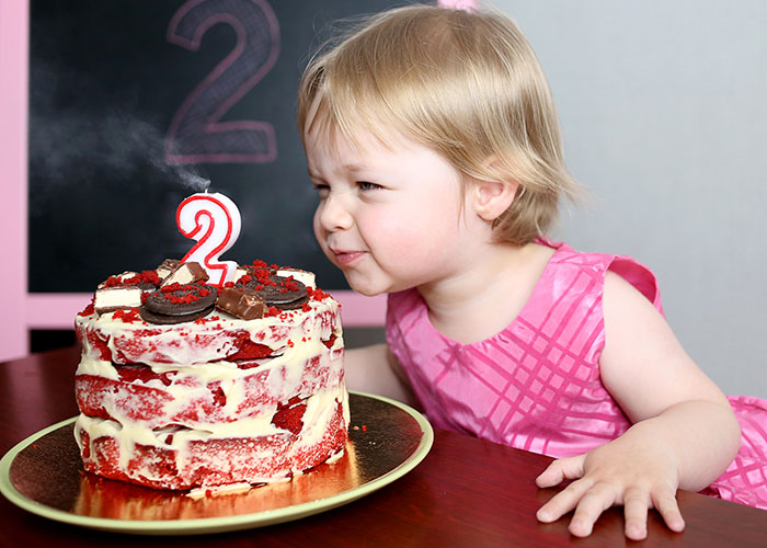 Toddler girl in pink dress celebrating birthday with a red velvet cake and number two candle at a kid&rsquo;s party.