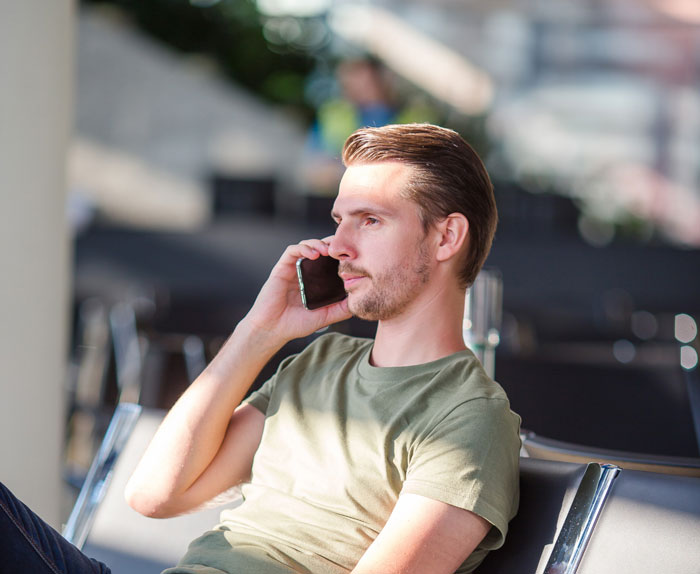 Young man talking on phone while waiting, representing entitled mother insists paying upgrade situation in public area.