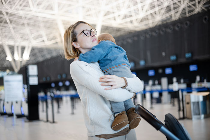 Mother holding baby at airport, showing entitled mother insists paying upgrade in travel setting.