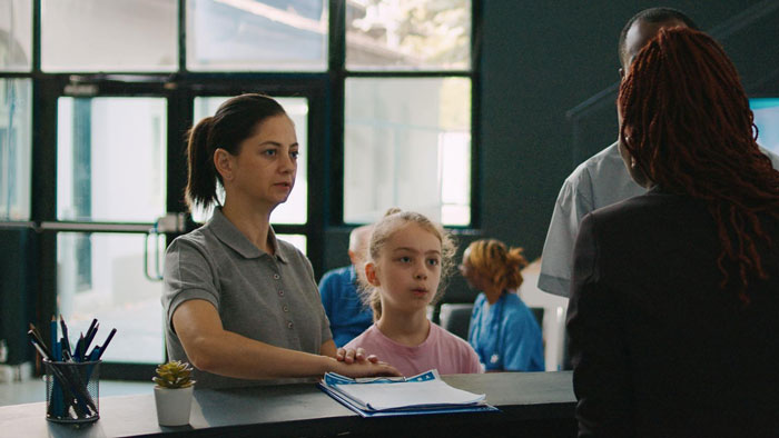 Mother with child at hotel front desk insisting on paying for an upgrade during check-in interaction.