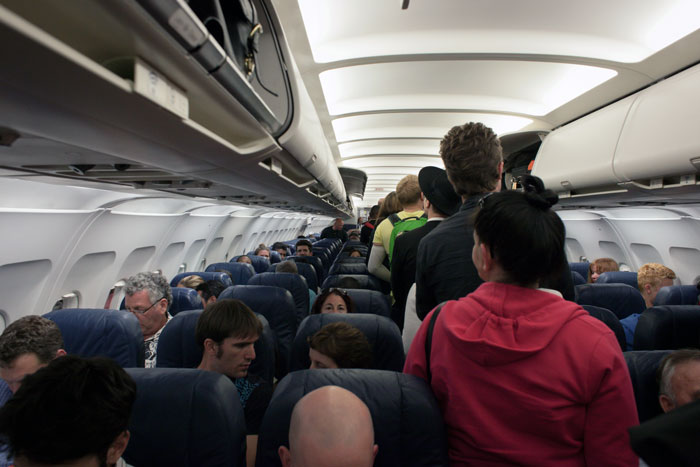 Passengers standing and seated inside a crowded airplane cabin as an entitled mother insists on paying for an upgrade.
