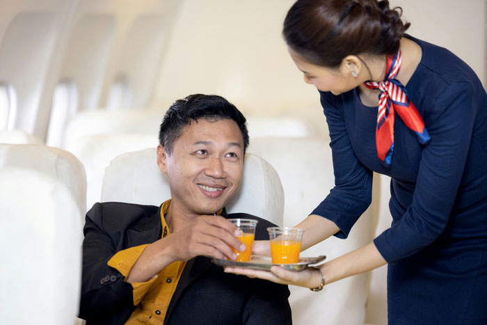 Flight attendant serving orange juice to a passenger on a plane as entitled mother insists on paying upgrade request.