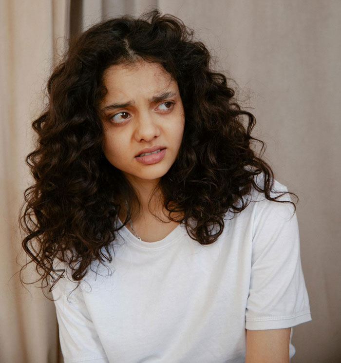 Woman with curly hair looking upset indoors, illustrating neighborhood drama over barking dog and garden dispute. Woman with curly hair looking upset indoors, illustrating neighborhood drama over barking dog and garden dispute.