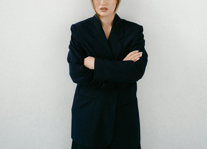 Woman in dark blazer stands with arms crossed, illustrating tension in neighborhood drama over barking dog complaint. Woman in dark blazer stands with arms crossed, illustrating tension in neighborhood drama over barking dog complaint.