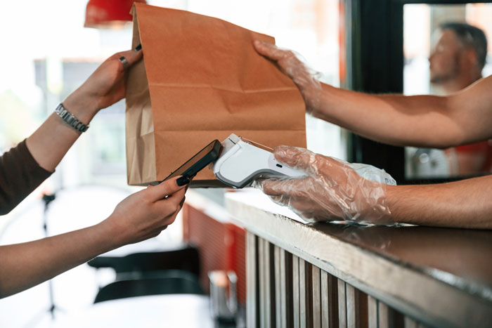 Customer trying to grab another guy&rsquo;s takeout at fast food counter where employee is holding a receipt machine.