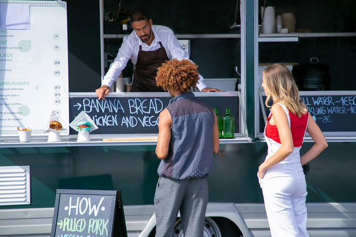 A lady tries to jump the line at a fast food truck while a man orders takeout from the vendor.
