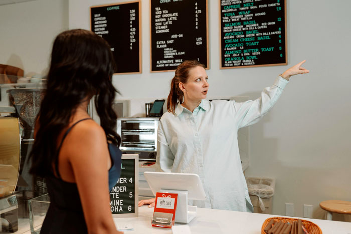 Customer tries to jump the line for fast food while staff member gestures toward the menu behind the counter.