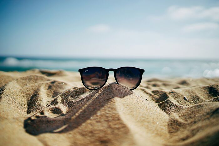 Sunglasses placed in sand on a beach with ocean in the background illustrating something normal that would shock Americans