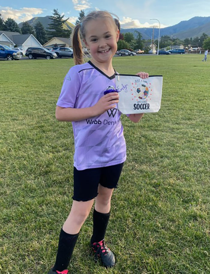 Young girl in soccer uniform smiling on field holding a small bag, related to missing sisters case and police search.
