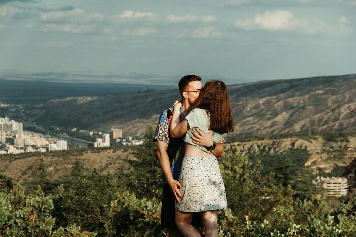 Couple embracing and kissing outdoors with mountains in the background, representing secrets people keep from their lovers.