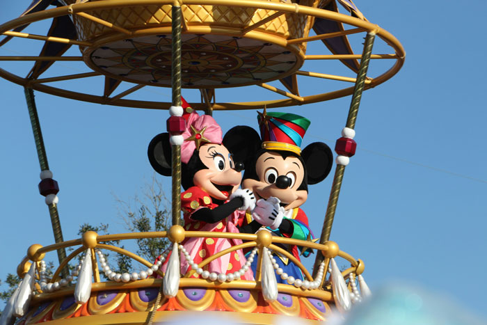 Mickey and Minnie Mouse in colorful costumes on a parade float with a clear blue sky background, family celebration theme.