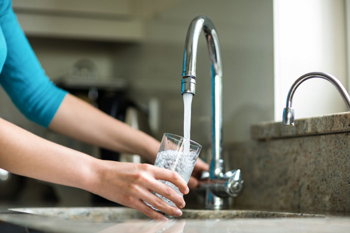Person filling a glass with water from a kitchen faucet, illustrating prolonged fasting effects and health risks.