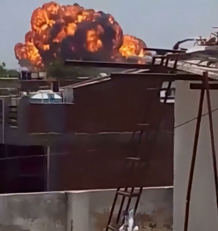 Explosion and fire following Air India plane crash near urban buildings captured in chaotic scene.