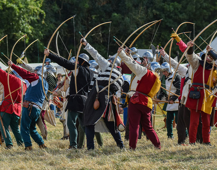 Group of historical reenactors in medieval attire drawing bows, illustrating common historical knowledge misconceptions.