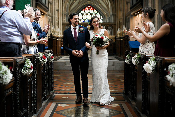 Bride and groom smiling and walking down the aisle of an elegant wedding ceremony with guests applauding.