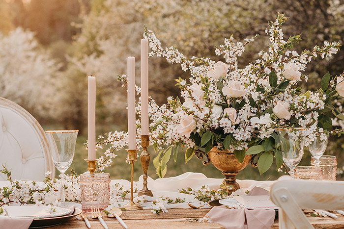 Elegant wedding table setting with floral centerpiece, candles, and glassware in an outdoor spring garden scene