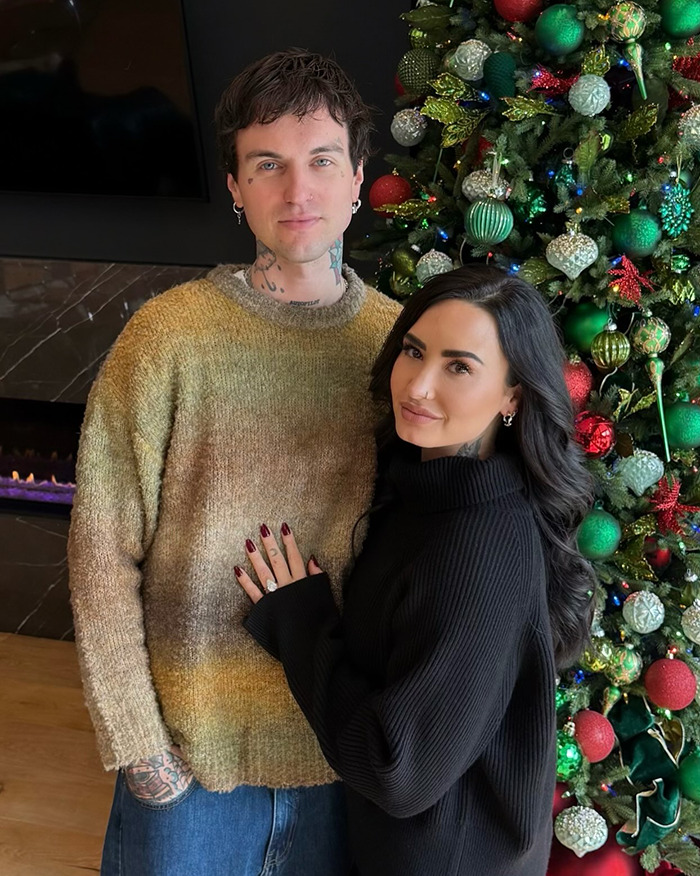 Couple posing by a decorated Christmas tree, highlighting famous lesbians who have gotten boyfriends in 2024 trend.