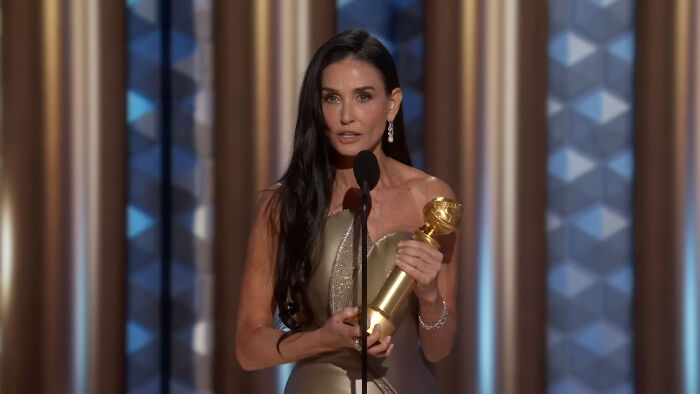 Actress holding award on stage, highlighting Hollywood hypocrisy about how women and men age differently.