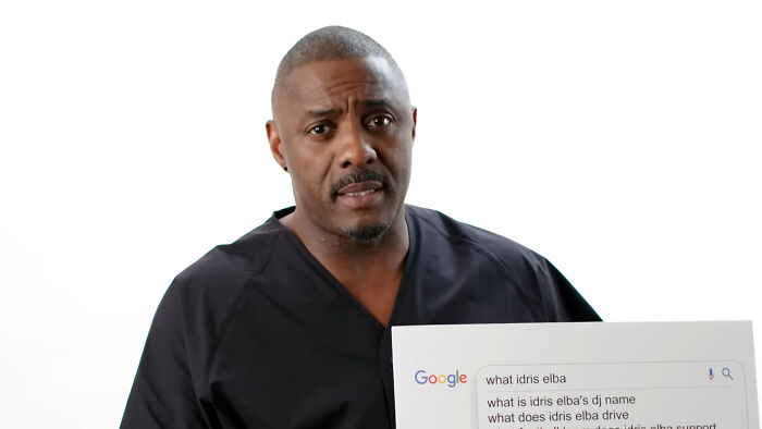 Idris Elba in a black shirt holding a Google search tablet discussing Hollywood hypocrisy about aging and gender.