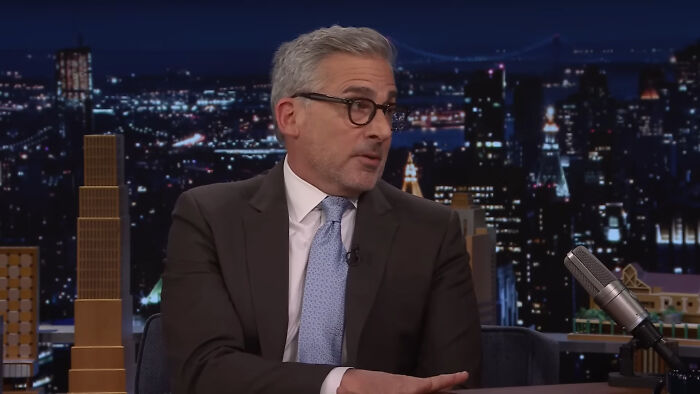 Man with gray hair and glasses wearing a suit on a late night talk show discussing Hollywood hypocrisy about aging.