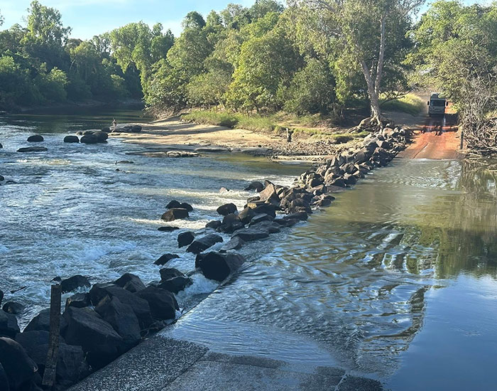 Man and child fishing on a quiet river with rocky banks near a shallow water crossing under sunlight. Man and child fishing on a quiet river with rocky banks near a shallow water crossing under sunlight.