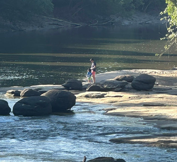Man and child fishing on a seemingly quiet river surrounded by rocks and trees, sparking heated reactions. Man and child fishing on a seemingly quiet river surrounded by rocks and trees, sparking heated reactions.