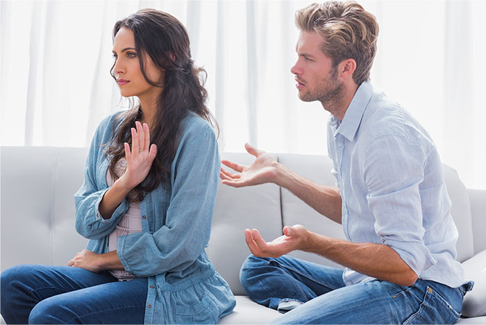 Man and woman having a tense argument on sofa, highlighting hurt feelings and relationship conflict about Mother's Day plans.