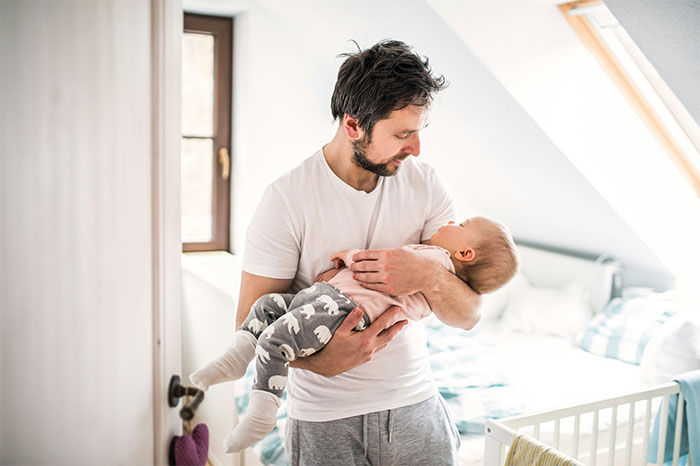 Man holding baby in a bright room, symbolizing family and emotions around Mother's Day hurt and relationships.