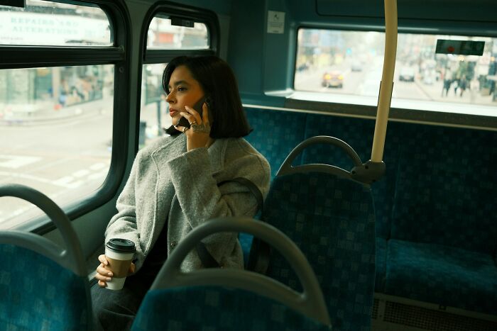 Woman on a bus holding coffee and talking on phone, reflecting on moments people realized a close friend was a jerk