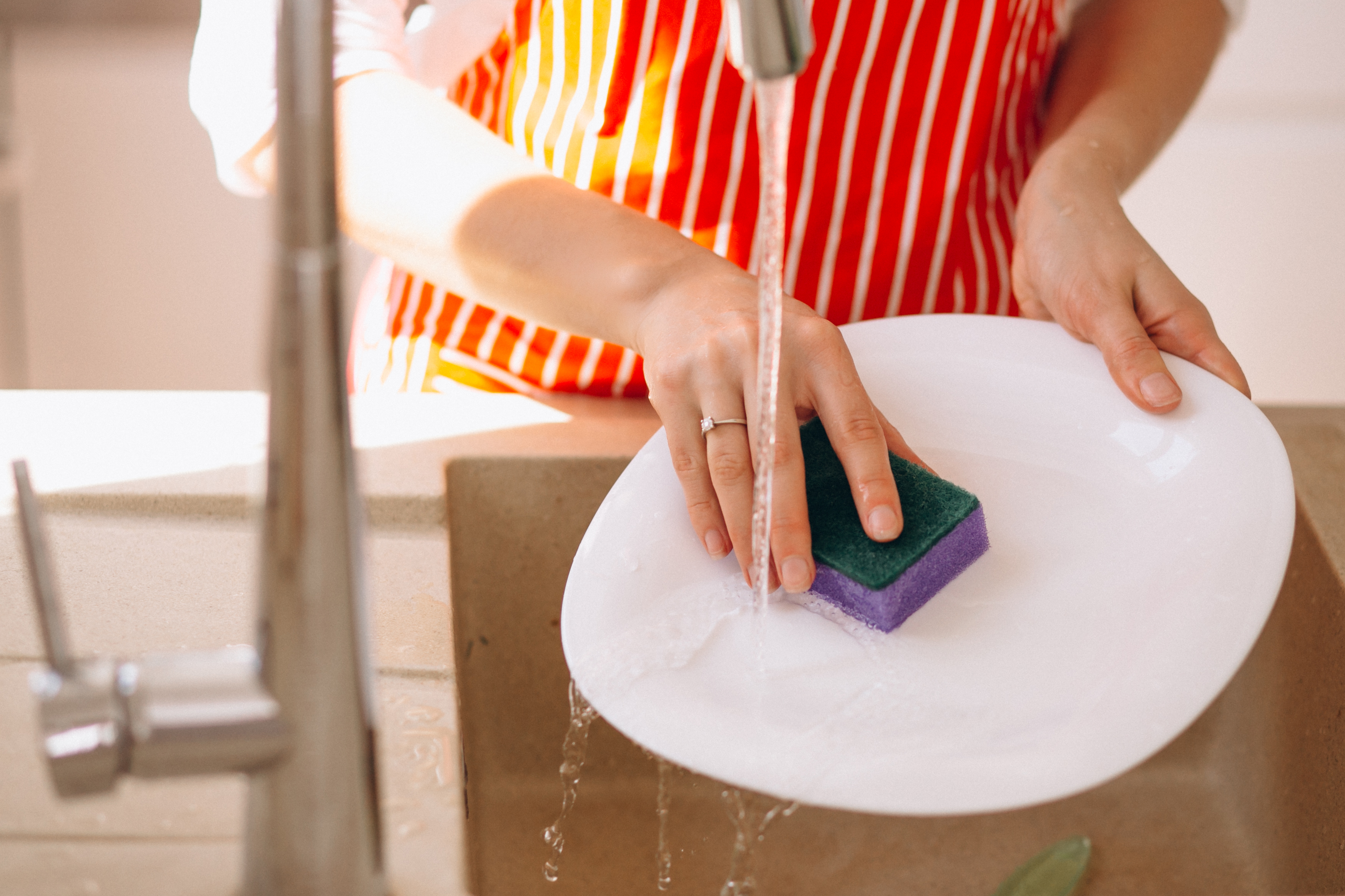 Woman standing her ground washing dishes with sponge under running water in kitchen sink at home. Woman standing her ground washing dishes with sponge under running water in kitchen sink at home.