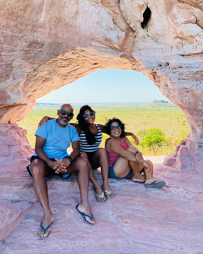 Three tourists sitting inside a natural rock arch with a scenic view, unrelated to being trapped inside an active volcano.