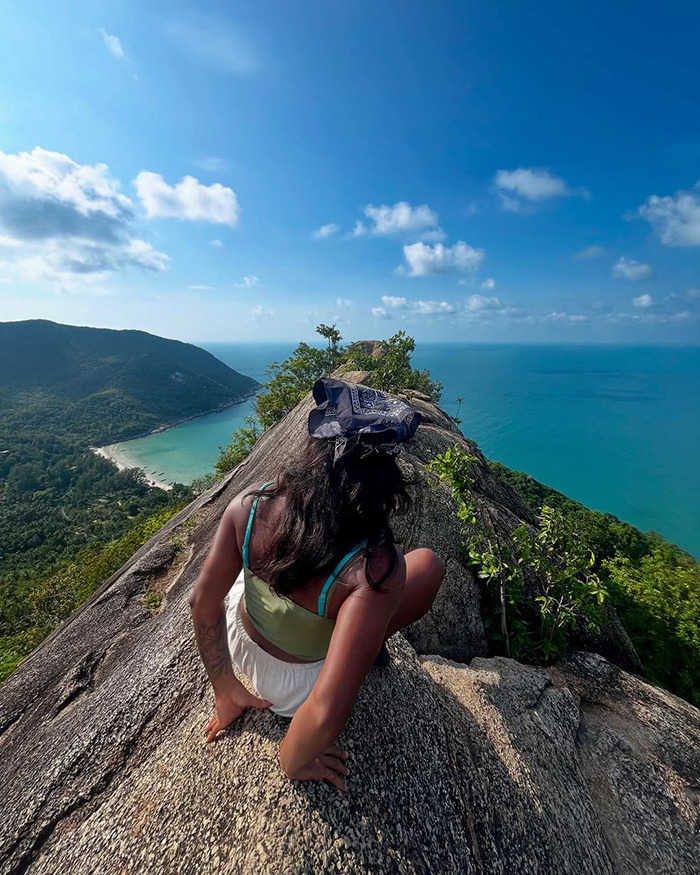 Woman sitting on rocky cliff overlooking ocean and green hills, symbolizing tourist trapped inside active volcano.