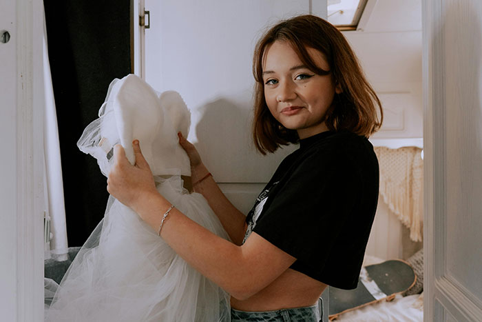 Bride holding a wedding dress indoors, reflecting on groom-to-be's cold feet jokes before their upcoming wedding.