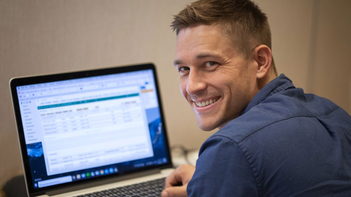 Young man controlling big money projects on laptop, smiling confidently while working in an office setting