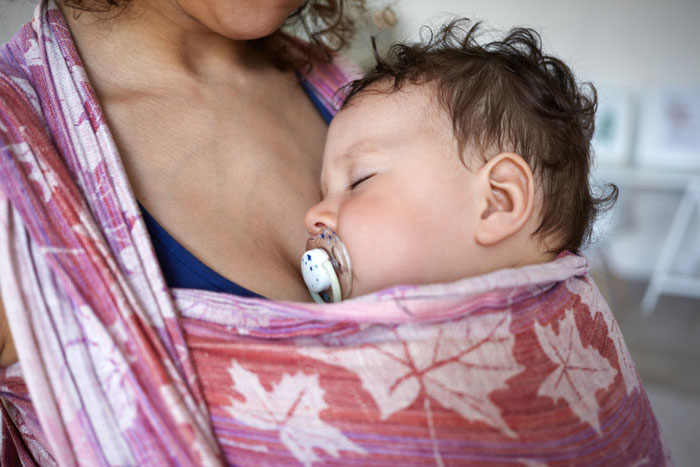 Mom breastfeeding baby wrapped in a pink sling, highlighting nursing and maternal care in a cozy setting. Mom breastfeeding baby wrapped in a pink sling, highlighting nursing and maternal care in a cozy setting.