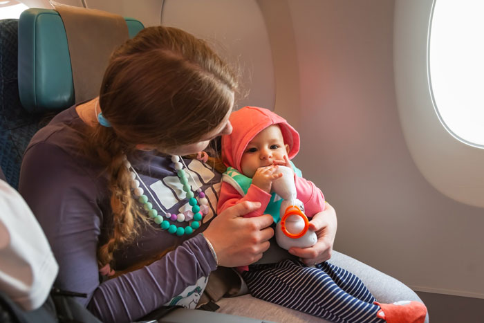 Mom nursing baby on airplane, holding infant with bottle, sitting by window seat during flight. Mom nursing baby on airplane, holding infant with bottle, sitting by window seat during flight.