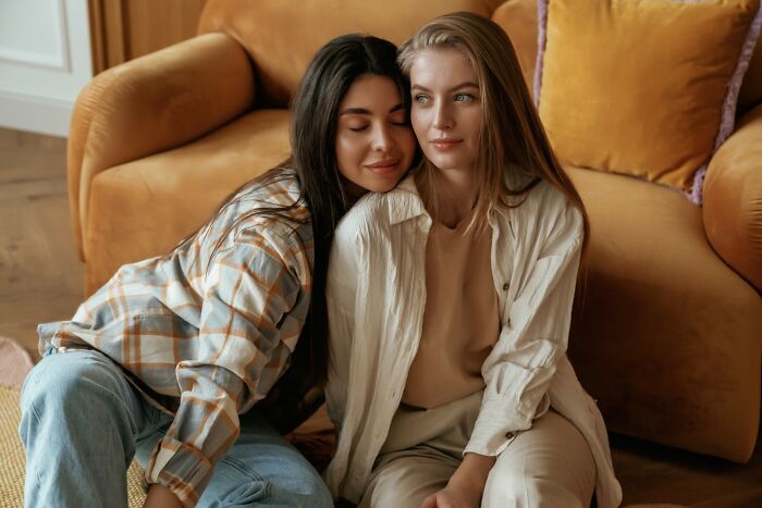 Two women sitting close together on the floor, sharing a comforting moment reflecting on deep secrets parents kept from kids.