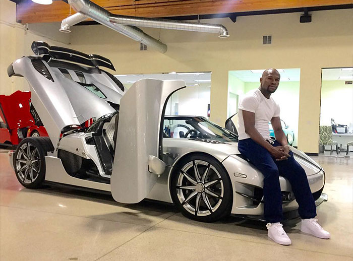 Floyd Mayweather sitting on a luxury sports car inside a garage showcasing his net worth and undefeated champ status.